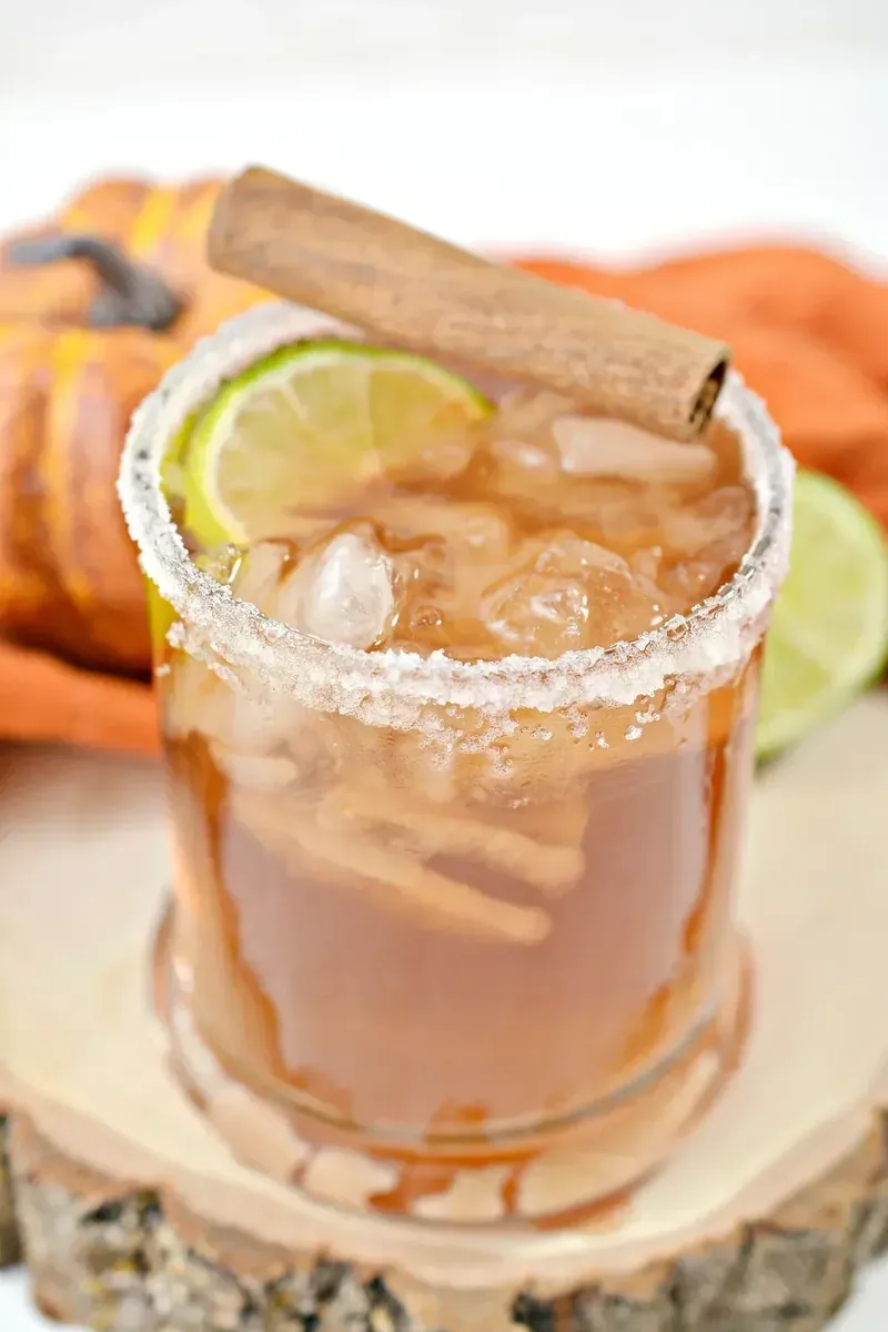 Keto thanksgiving margarita with lime wedge and cinnamon stick on wood coaster