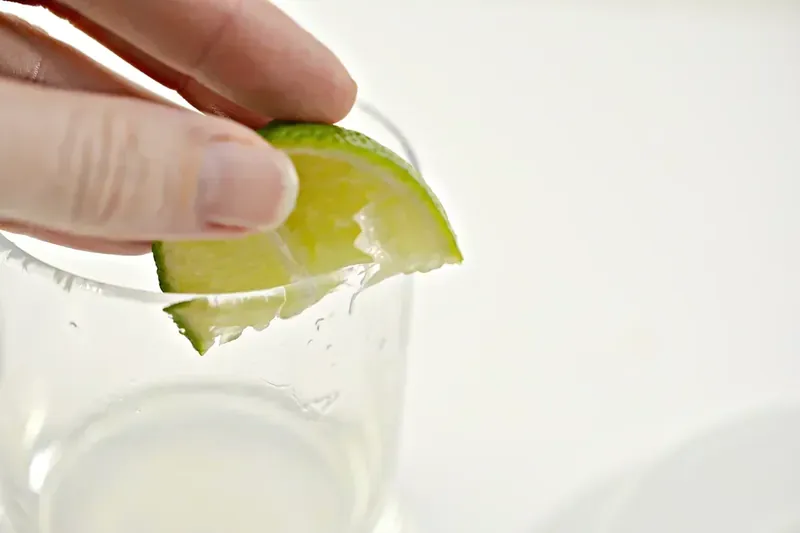 Lime wedge being rubbed around glass rim for margarita preparation
