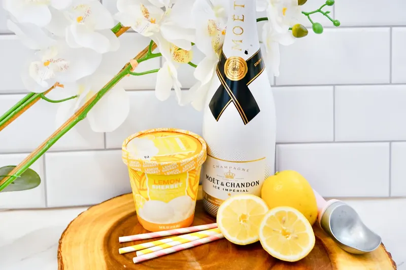 Champagne bottle, lemon sorbet, fresh lemons and ice cream scoop on wooden board