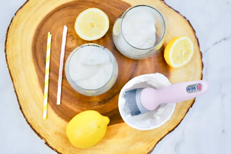 Ice cream scoop adding lemon sorbet to wine glasses with lemon slices nearby