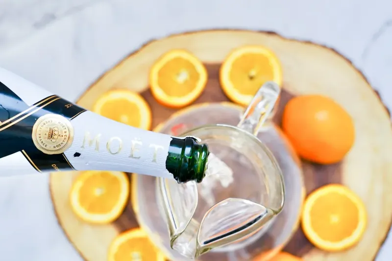 Champagne being poured into glass pitcher for mimosa sangria