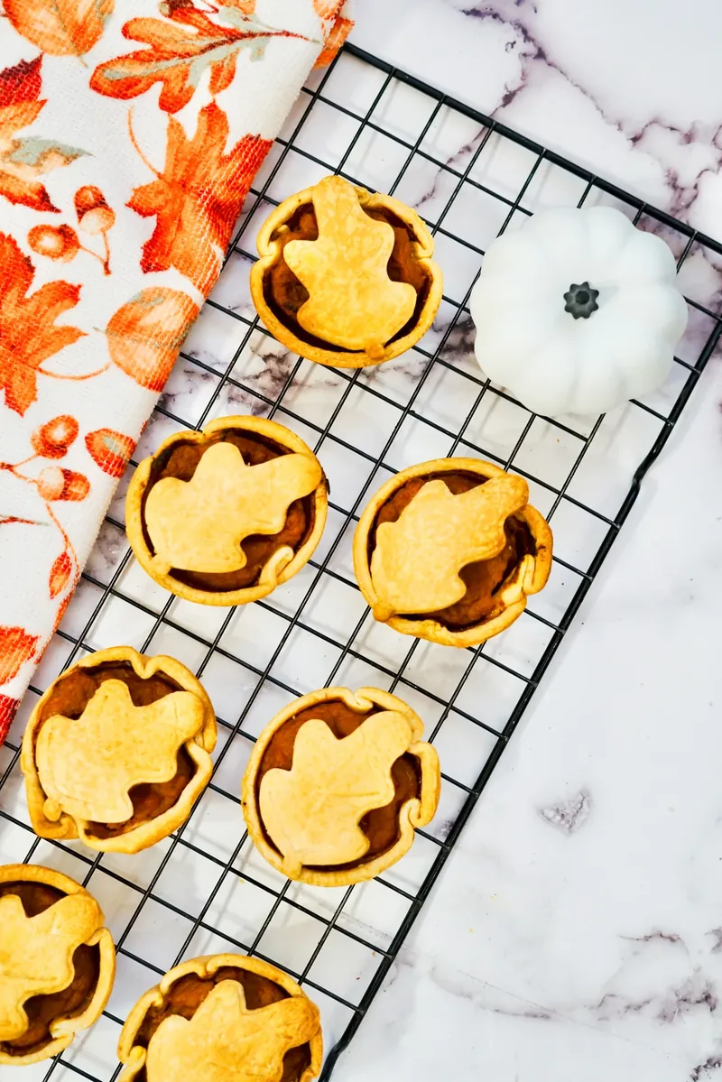 Mini pumpkin pies displayed on cooling rack with autumn decorative towel