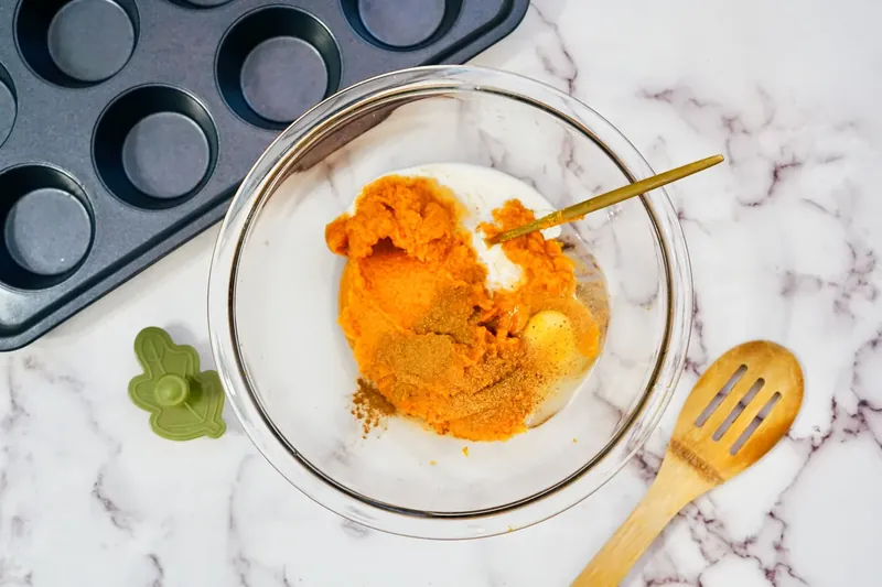 Pumpkin pie filling being mixed in glass bowl with spoon