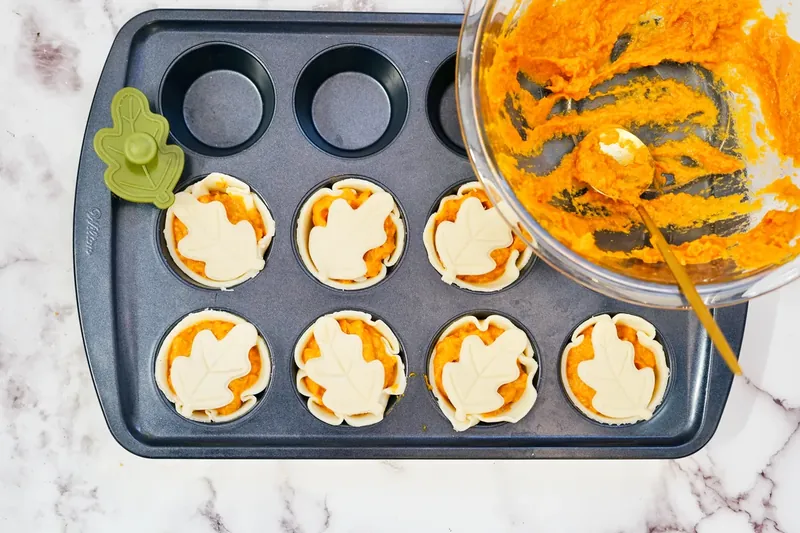 Leaf-shaped pastry cutouts being placed on top of mini pumpkin pies