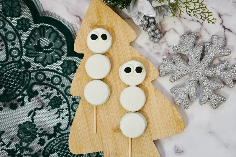Oreo snowmen with candy eyes attached to top cookies using frosting as adhesive