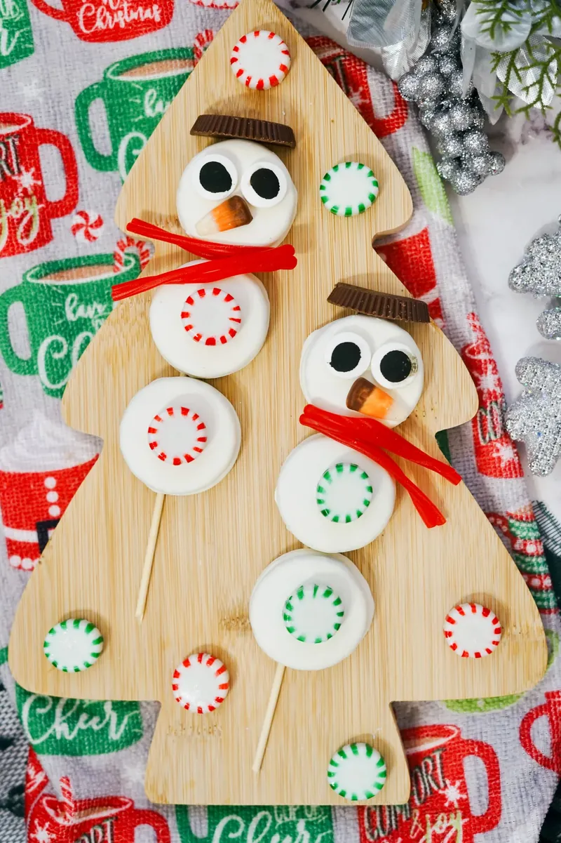 Final display of Oreo snowmen skewers arranged on festive Christmas tree shaped cutting board with holiday decorations