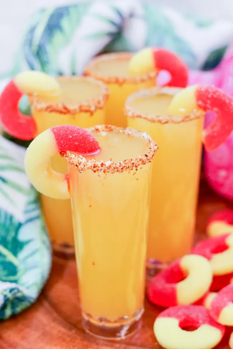 Golden peach margarita shooters with Tajin rim and peach ring garnishes