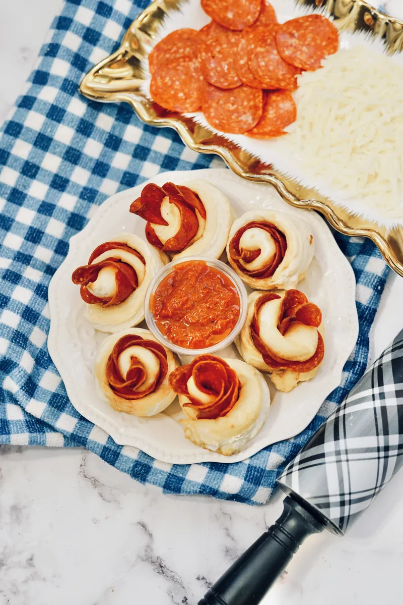 Gourmet pepperoni rose balls with marinara sauce on white plate alongside gold tray with fresh ingredients