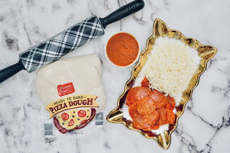 Pizza dough, pepperoni, mozzarella cheese, pizza sauce and rolling pin for pepperoni rose balls