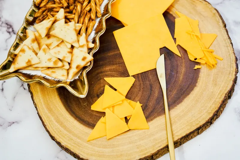 Cutting cheddar cheese into triangles using crackers as stencils on wooden board