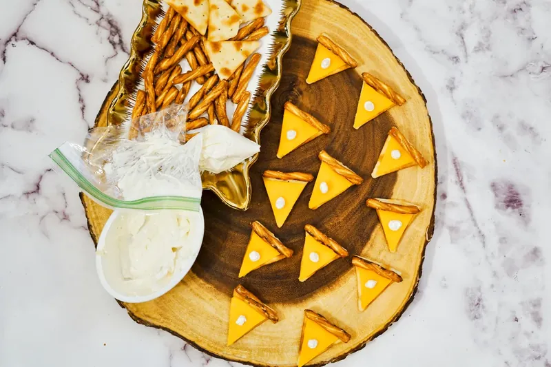 Piping cream cheese dots onto pie-shaped cheese crackers for whipped cream effect