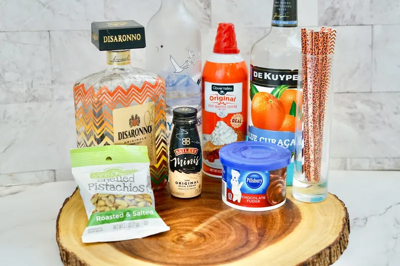 All ingredients for pistachio martini arranged on wooden board including liqueurs, pistachios, and chocolate frosting