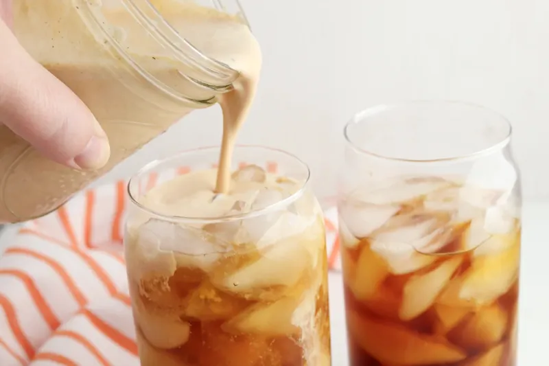 Hand pouring pumpkin sweet cream into iced cold brew coffee