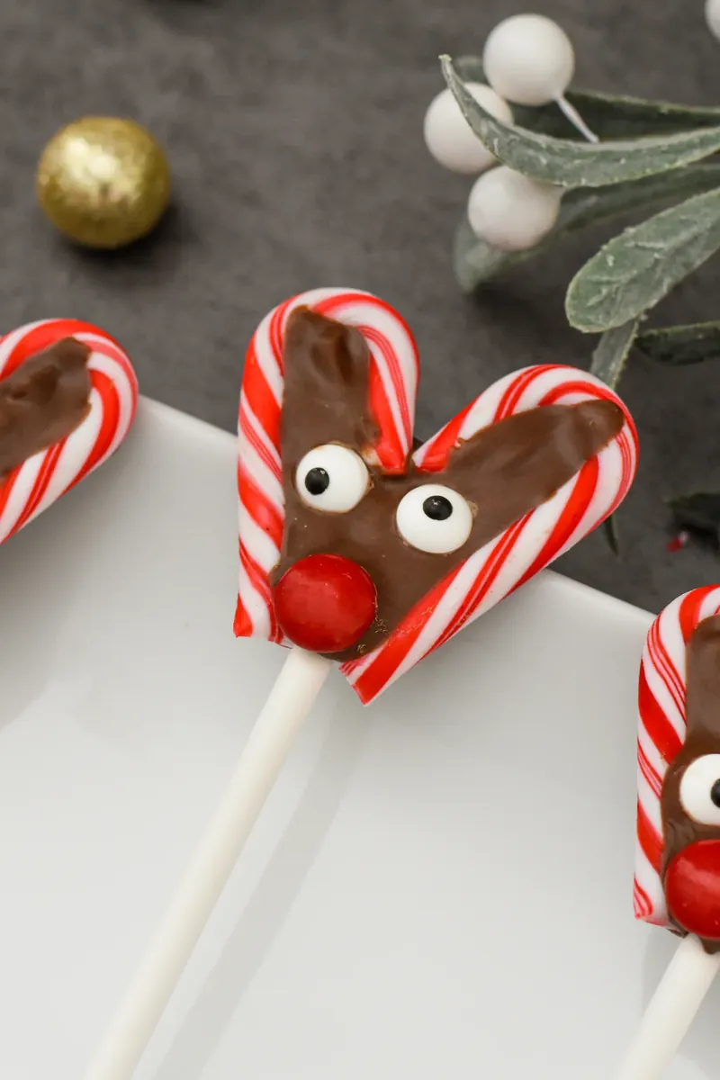 Finished reindeer candy cane pops displayed with holiday decorations and ornaments for Christmas
