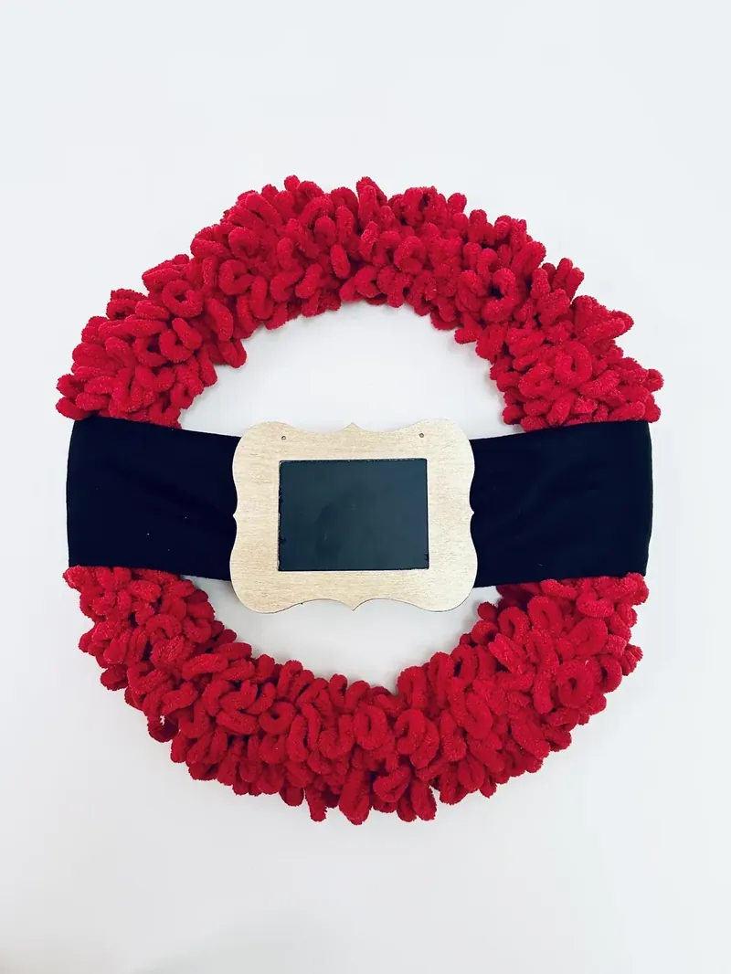 Completed Santa belt wreath laid flat showing red yarn wreath with black fleece belt and gold chalkboard buckle