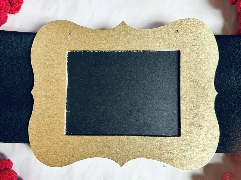 Completed belt buckle with gold painted frame attached to center of black fleece scarf belt