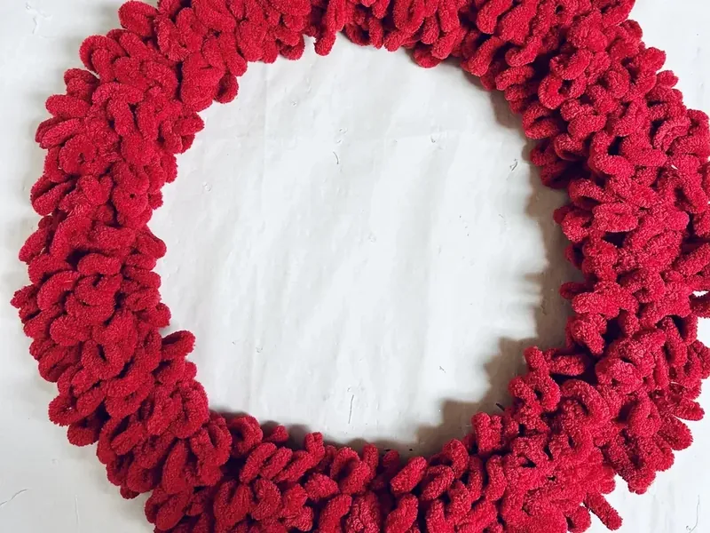 Wire wreath form completely covered in red textured yarn creating full circular wreath base