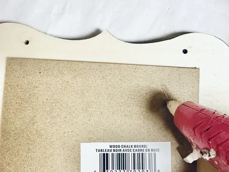 Hot glue gun applying glue to back of gold painted chalkboard frame before attaching to black fleece