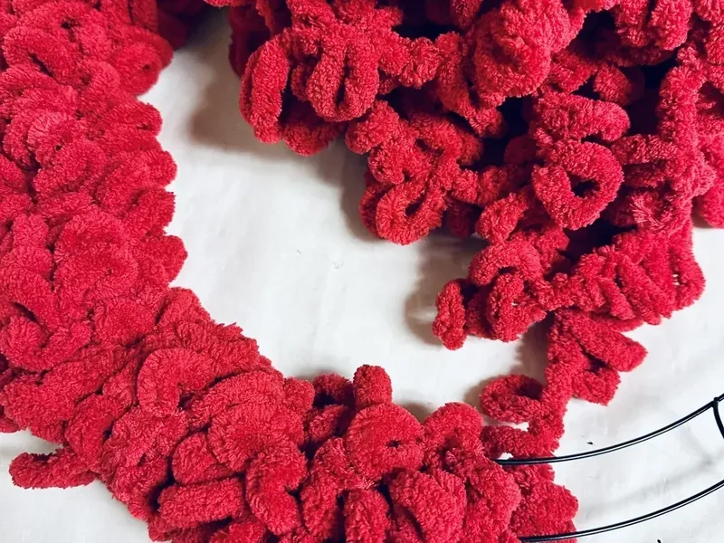 Wire wreath form being wrapped with red textured yarn showing partial coverage