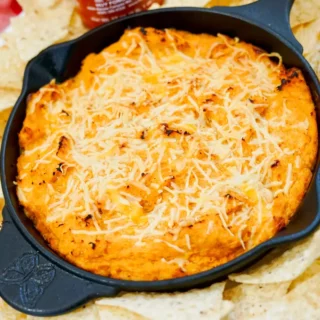 Golden baked honey sriracha chicken dip in cast iron skillet with tortilla chips