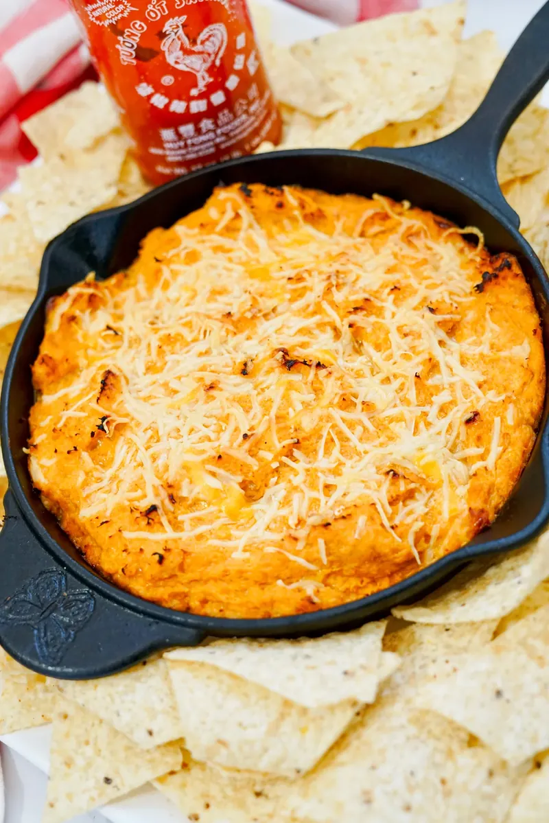 Golden baked honey sriracha chicken dip in cast iron skillet with tortilla chips