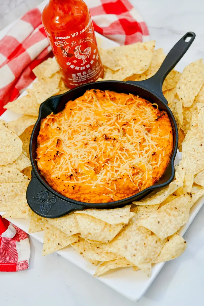 Honey sriracha chicken dip presentation with sriracha bottle and tortilla chips