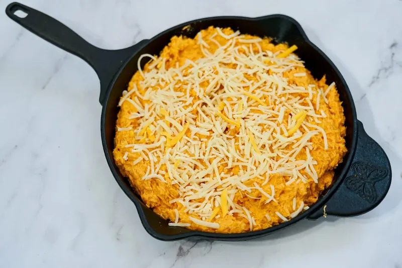 Overhead view of prepared honey sriracha chicken dip in cast iron skillet before baking