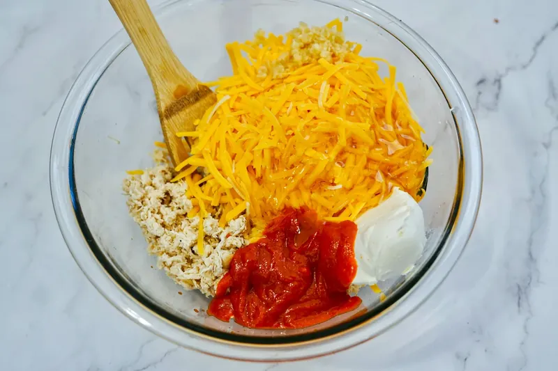 Mixing bowl with shredded chicken, cream cheese, cheddar cheese, and sriracha honey sauce