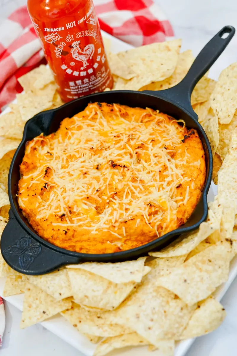 Baked honey sriracha chicken dip served with tortilla chips around cast iron skillet