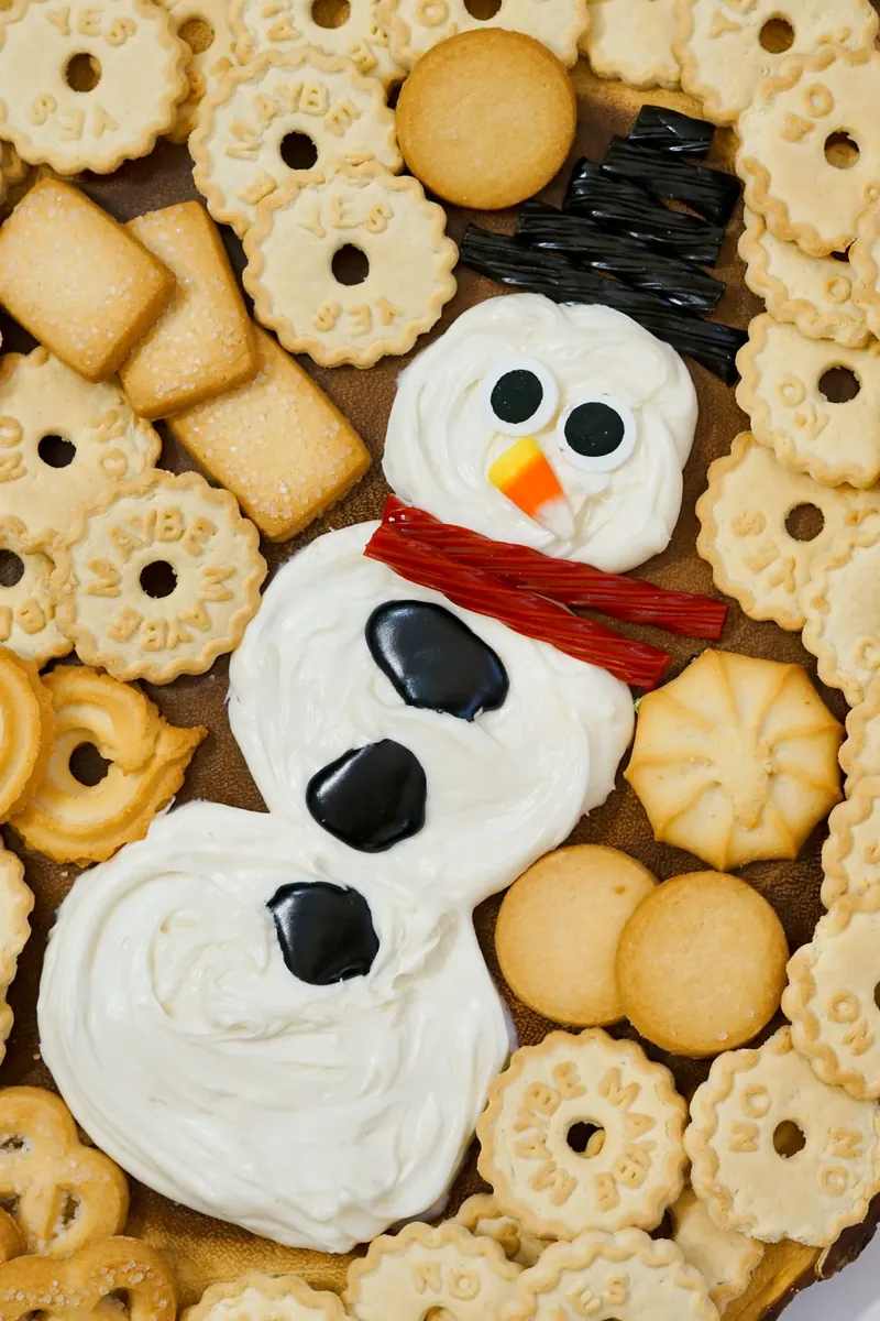 Finished snowman frosting board with various cookies and crackers arranged around decorated snowman