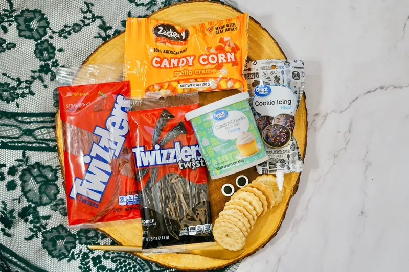 Ingredients for snowman frosting board including candy corn, Twizzlers, cream cheese frosting, black icing, and candy eyes on wooden board