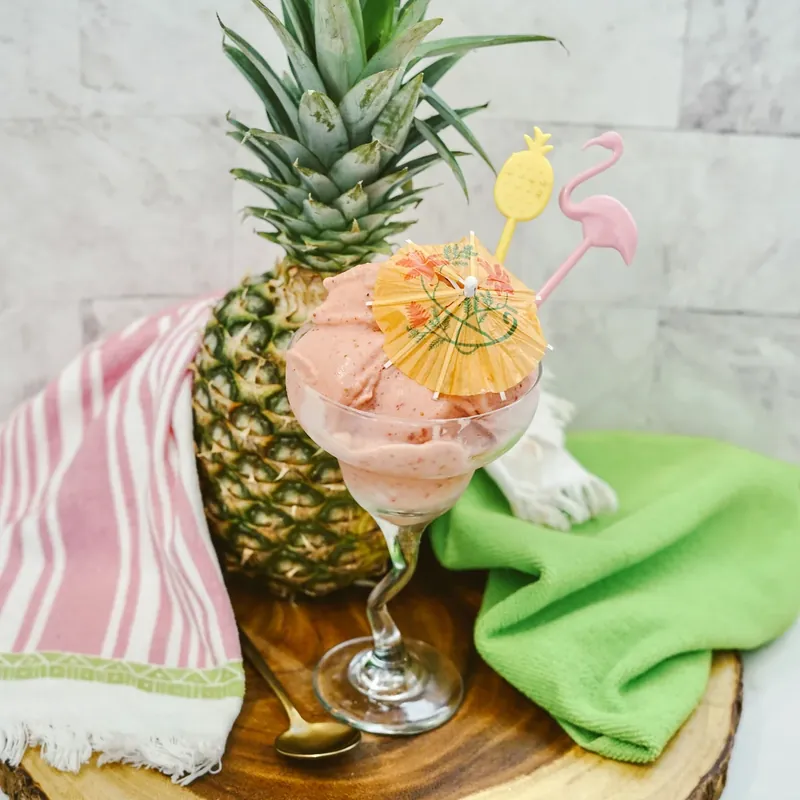 Close up of strawberry dole whip in glass with decorative paper umbrella