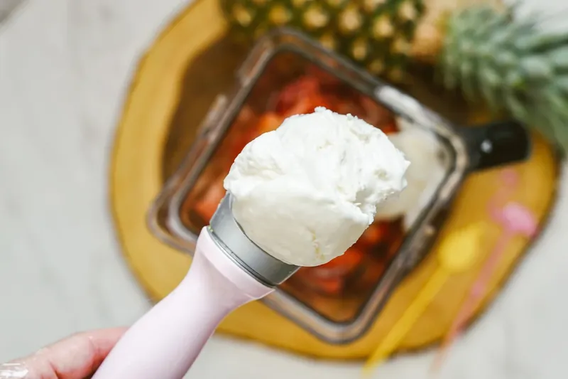 Hand adding vanilla ice cream to blender with frozen strawberries