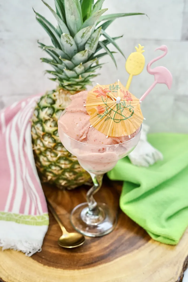 Strawberry dole whip in margarita glass with tropical styling and pineapple background