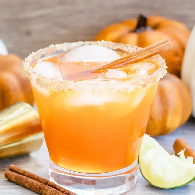 Apple cider margarita with brown sugar rim and autumn pumpkin backdrop