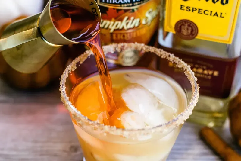 Pouring apple cider and liquors into margarita glass with ice