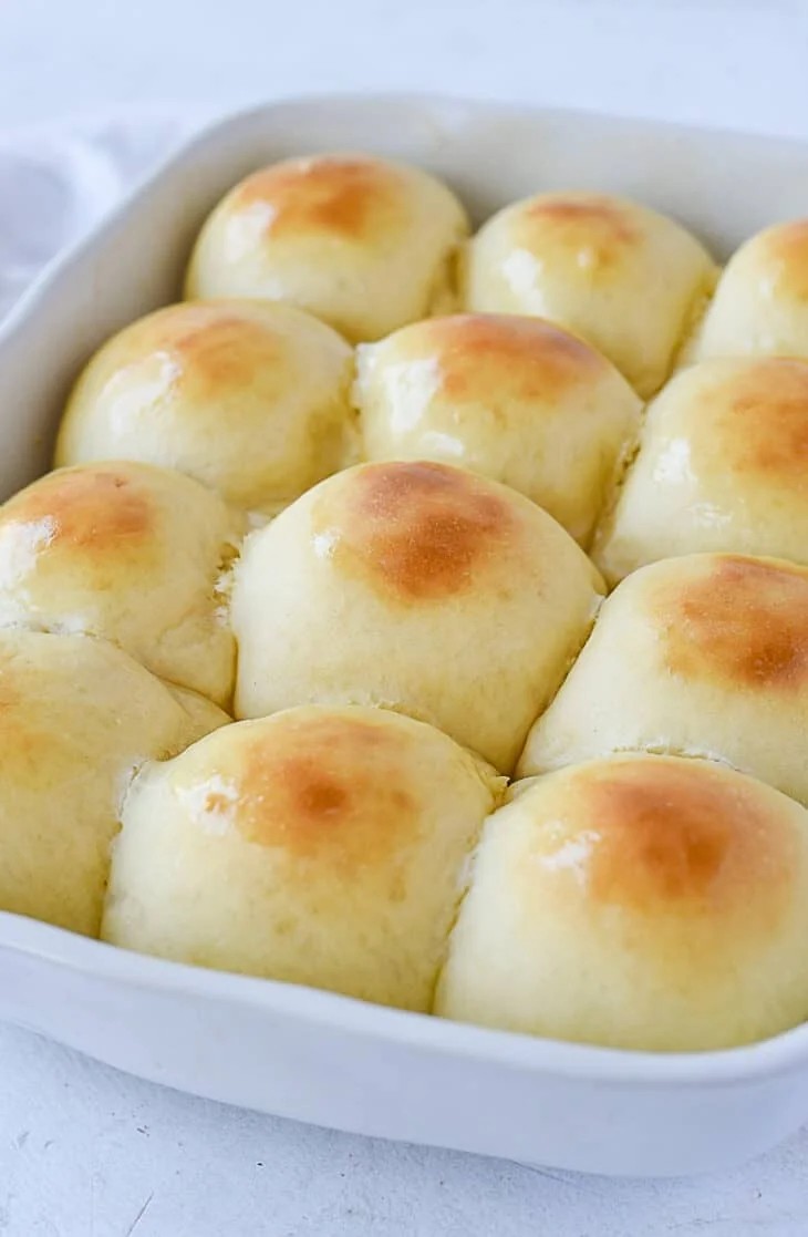 golden brown homemade dinner rolls baked together in white ceramic baking dish