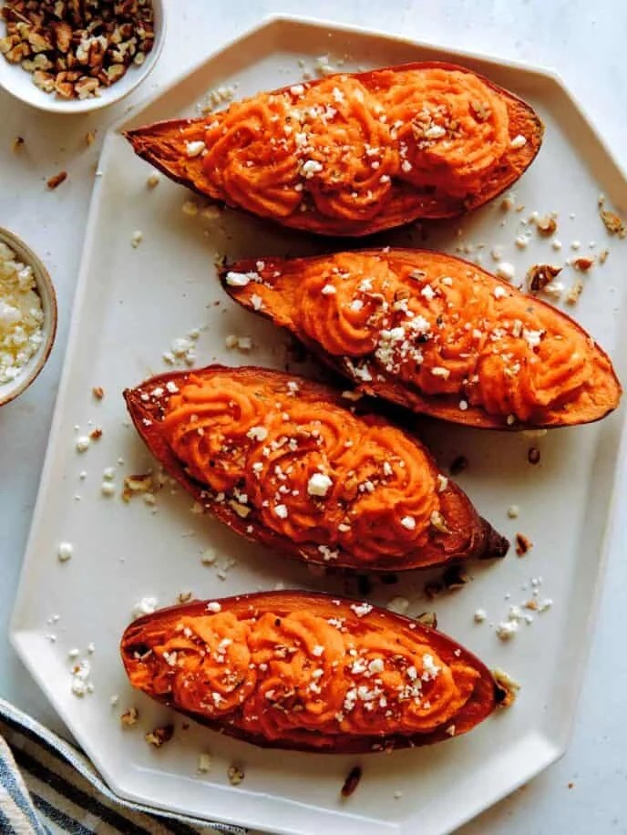 roasted sweet potato halves topped with crumbled feta cheese and nuts on baking sheet