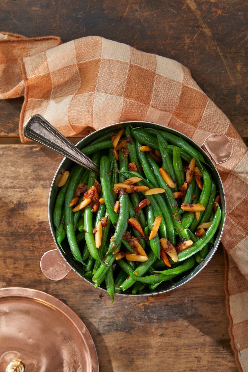 sautéed green beans with sliced almonds in copper serving pan with wooden spoon