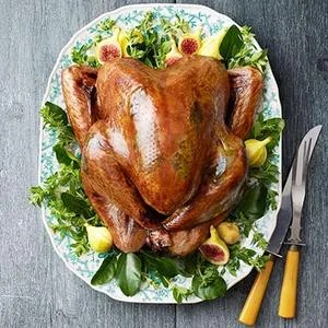 golden roasted whole turkey garnished with fresh herbs and lemon on white platter
