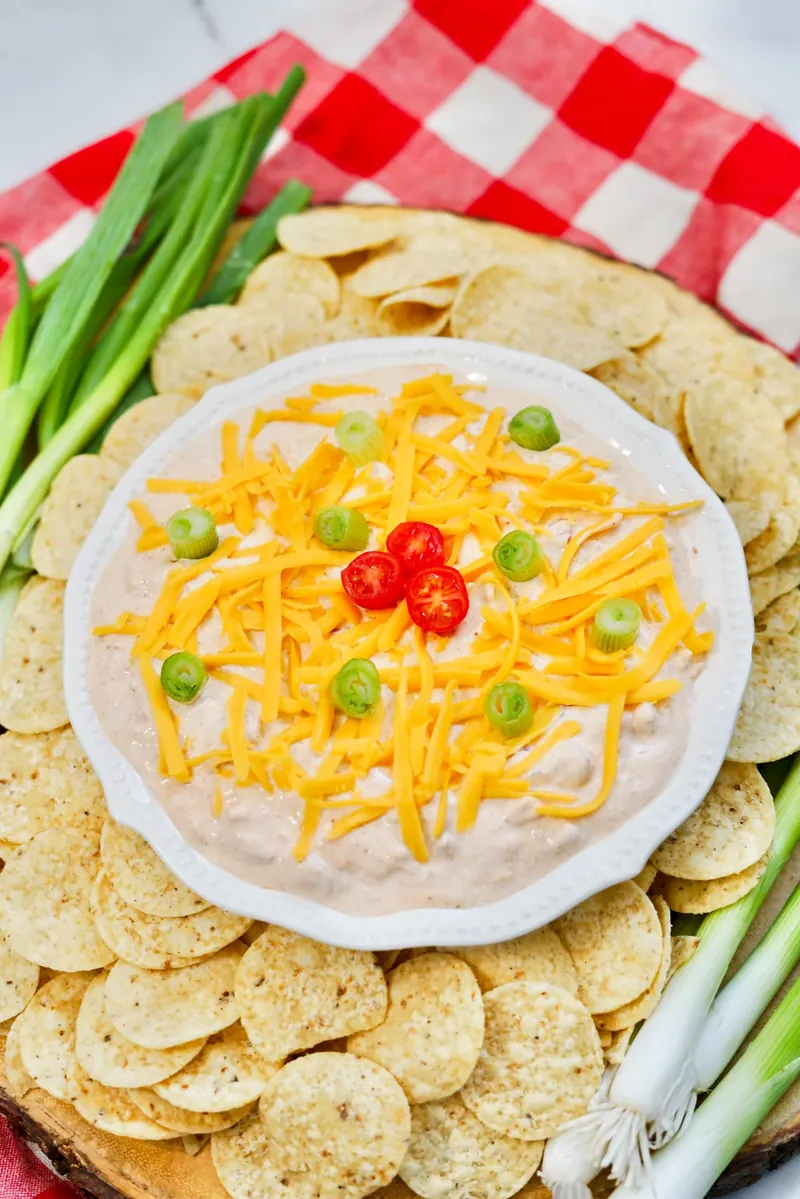 Overhead view of TikTok boat dip with bright orange cheese, green onions, and red tomatoes