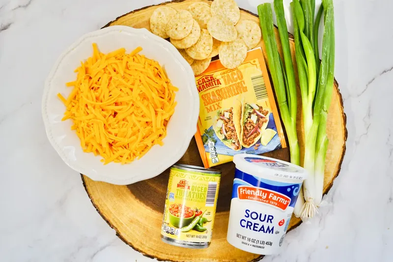 Ingredients for TikTok boat dip including sour cream, RoTel, cheddar cheese, taco seasoning, tortilla chips, and green onions