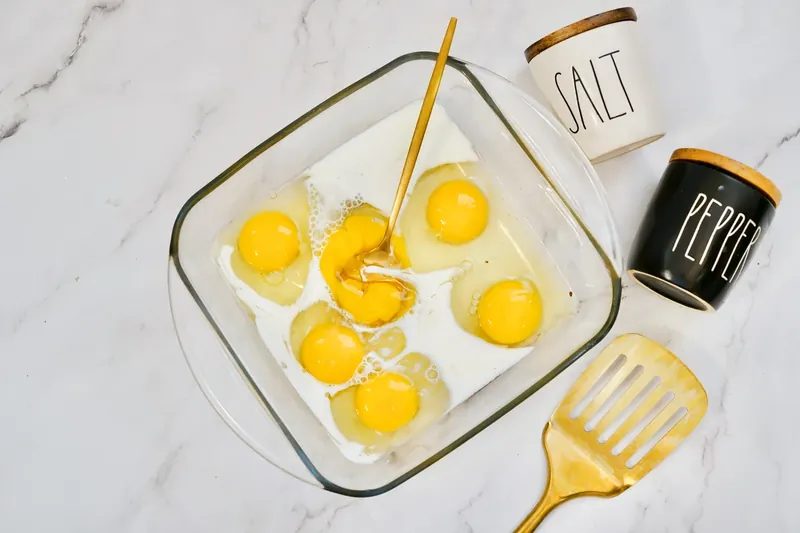 Eggs and milk being whisked together in glass baking dish