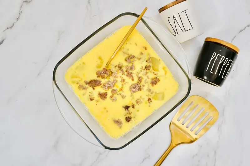 Cooked breakfast sausage being stirred into egg mixture in baking dish