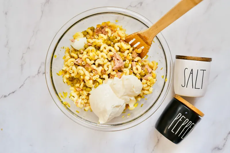 Wooden spoon mixing mayonnaise into tuna mac salad ingredients