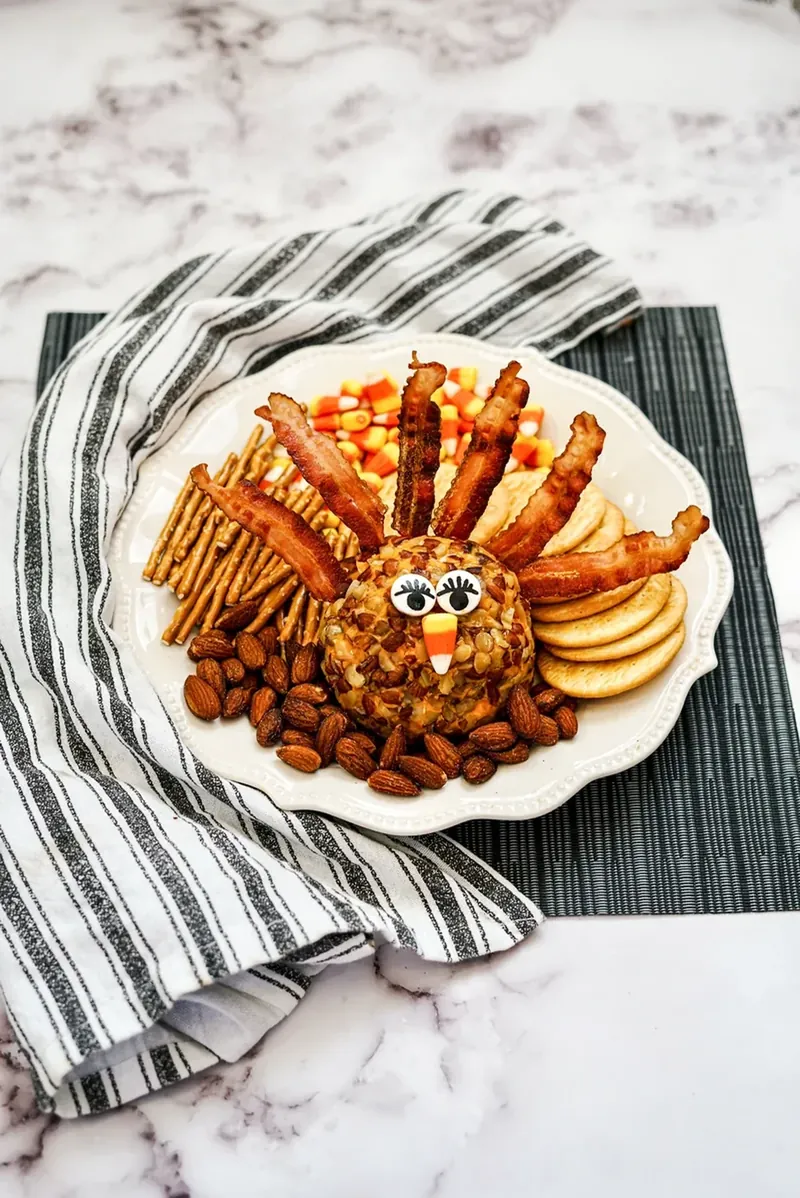 Turkey cheese ball appetizer with bacon feathers and candy corn on striped napkin