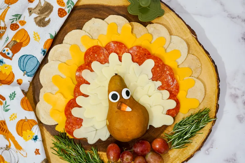 Close-up of turkey cheese plate showing pear body with candy eyes and jellybean beak