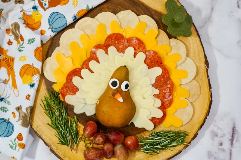 Thanksgiving turkey cheese and charcuterie plate with layered cheese feathers, pepperoni, pear turkey body, and grape garnish on wooden board