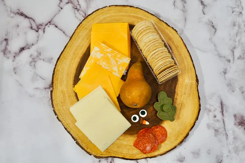 Ingredients for turkey cheese plate including cheddar cheese, crackers, pear, candy eyes, and pepperoni