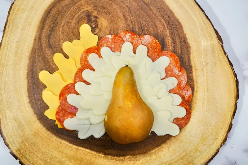 Turkey-shaped cheese and pepperoni arrangement with pear body on wooden serving board